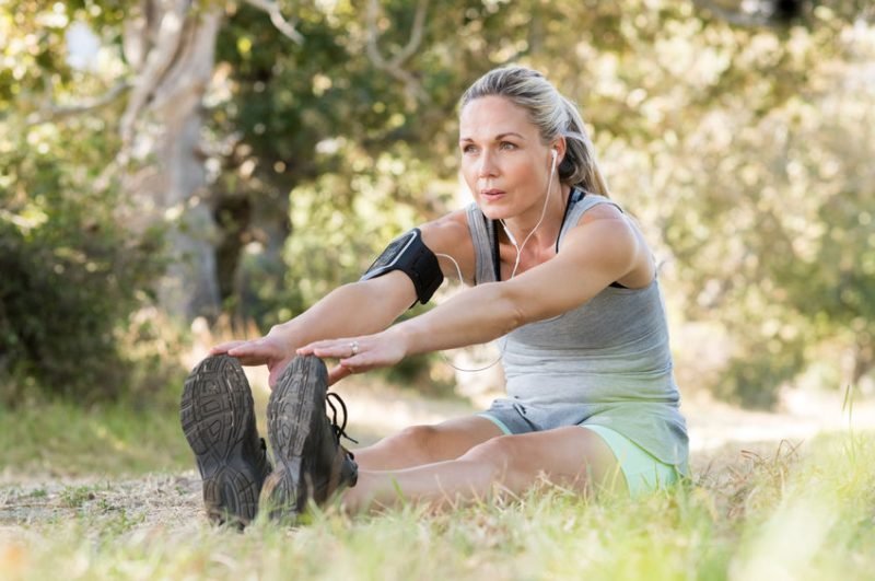 Senior woman exercising in park while listening to music. Senior woman doing her stretches outdoor. Athletic mature woman stretching after a good workout session.